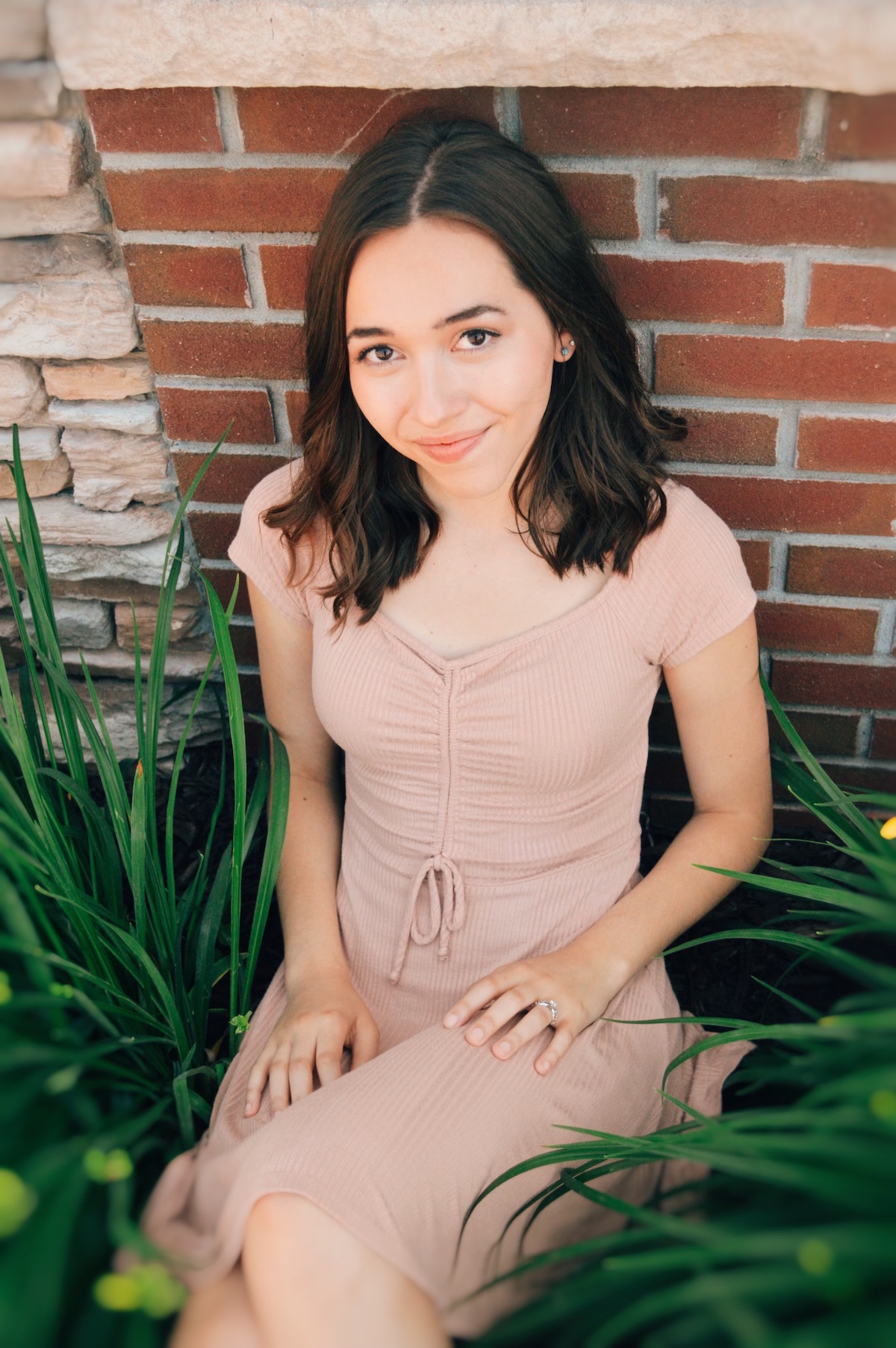 Eva sitting amongst plants against a brick wall.